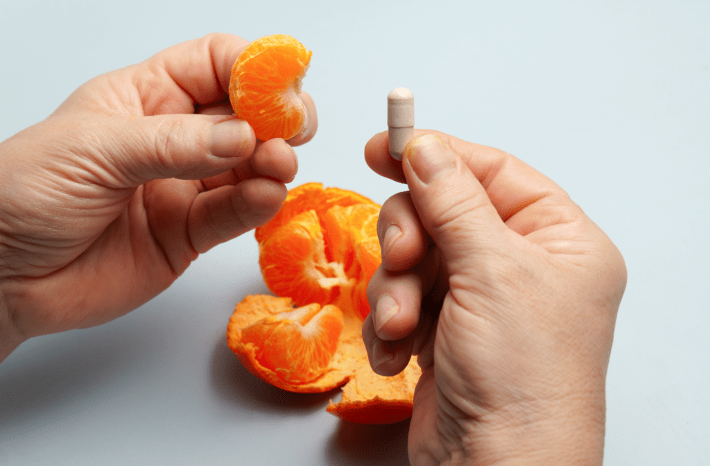 Mandarine und Vitamin C Kapsel als Symbol für die Frage, ob Vitamin C besser über die Ernährung oder über Nahrungsergänzungsmittel aufgenommen werden sollte.