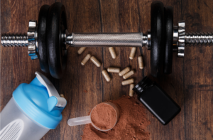 Hantel, Trinkflasche und Nahrungsergänzungsmittel auf Holzuntergrund als Symbol für Sport, Muskelaufbau und Supplements
