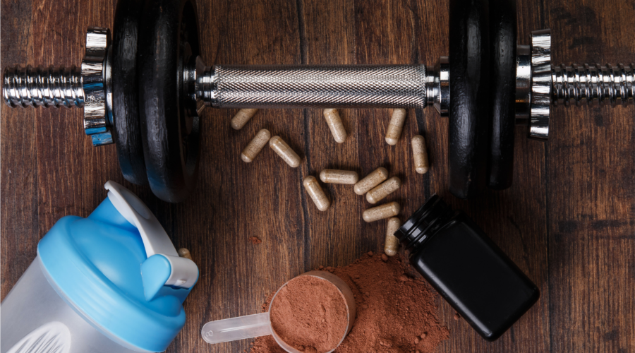Hantel, Trinkflasche und Nahrungsergänzungsmittel auf Holzuntergrund als Symbol für Sport, Muskelaufbau und Supplements