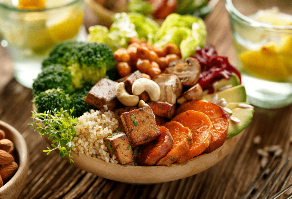 Bunte Bowl mit Tofu, Quinoa, Kichererbsen, Brokkoli, Süßkartoffeln, Avocado, Pilzen und Cashewkernen.