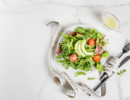 Teller mit Blattsalat, Avocado und Tomaten neben einem Maßband und Besteck auf einem hellen Tisch.