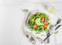 Teller mit Blattsalat, Avocado und Tomaten neben einem Maßband und Besteck auf einem hellen Tisch.